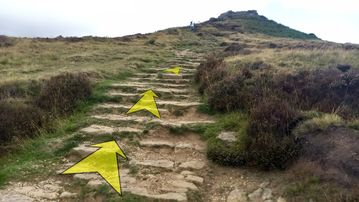 A photo of step 33 of the Burbage Rocks & Higger Tor Walk route, with yellow arrows superimposed to show the way.
